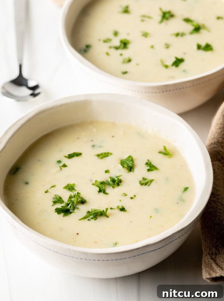 Two white bowls with homemade cream of chicken soup, generously garnished with fresh chopped parsley.