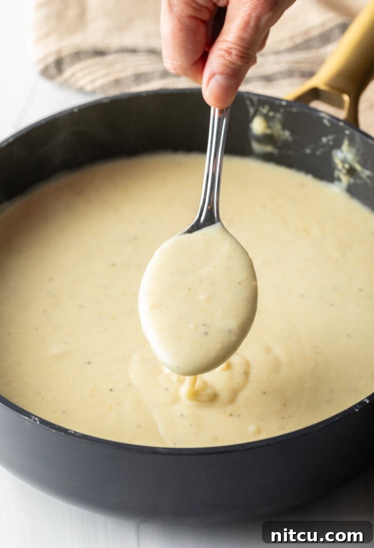 Large cooking pot with a rich, creamy soup being stirred by a large metal spoon, mid-preparation.