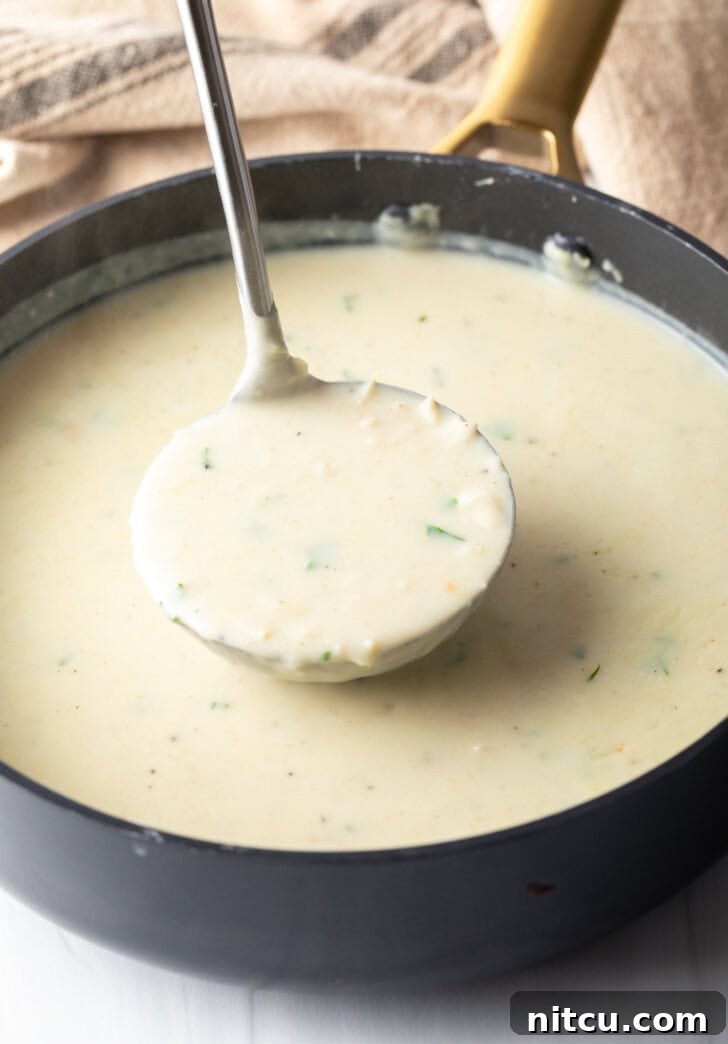 Large cooking pot filled with creamy chicken soup, being stirred by a metal ladle just before serving.