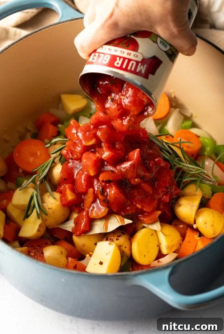 Hand adding canned diced tomatoes to the pot with fresh veggies.