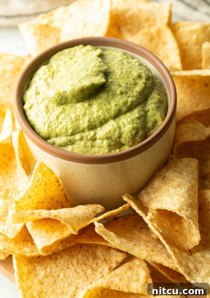 Small bowl of poblano cream sauce surrounded by tortilla chips.