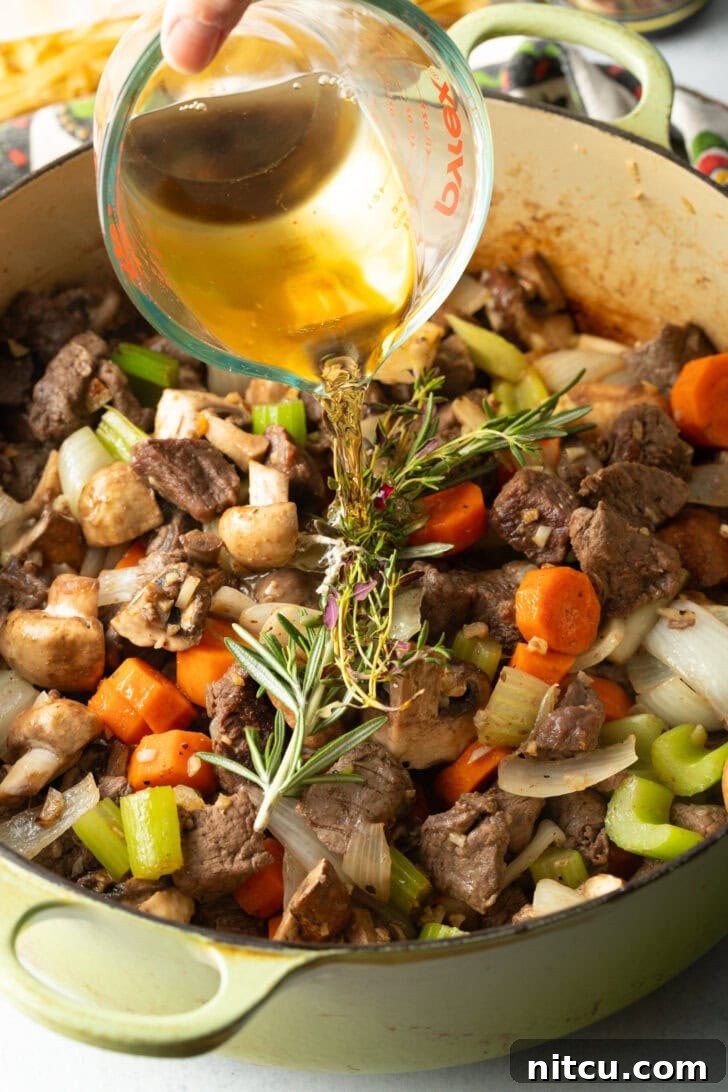 Searing beef chunks and veggies in a large cooking pot. Adding sprigs. Pouring in broth