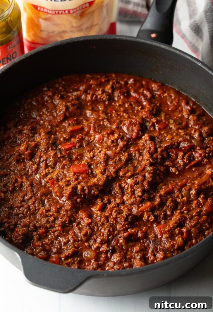 A close-up shot of a deep, black cast iron skillet filled with freshly made, rich, and hearty homemade chili. The chili has a thick consistency, with visible chunks of meat and vegetables, ready to be served.
