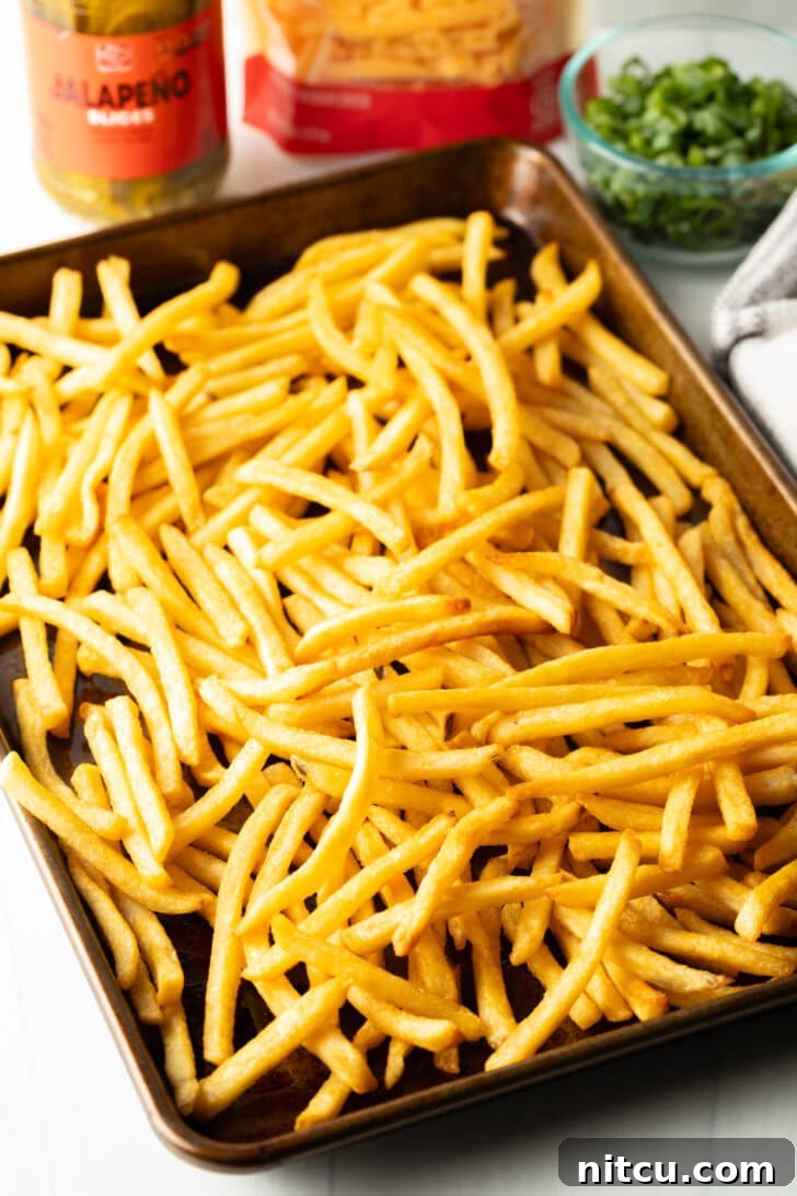 A large baking sheet generously loaded with golden, crispy french fries, fresh out of the oven or fryer. They appear perfectly cooked and seasoned, ready for assembly.