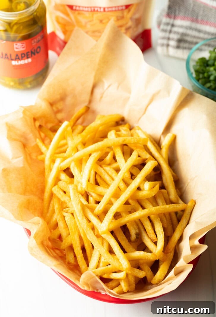 A rustic basket lined with parchment paper, filled with a generous portion of freshly cooked, golden, and crispy french fries, ready for the delicious toppings.
