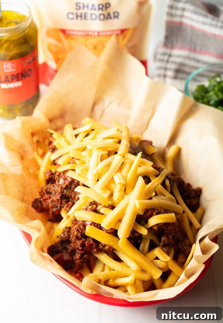 A rustic basket lined with parchment paper, filled with crispy french fries generously topped with a rich, hot chili and a lavish sprinkling of shredded cheddar cheese, which has just begun to melt.