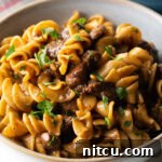White bowl with a generous serving of beef and noodles, topped with fresh chopped parsley.