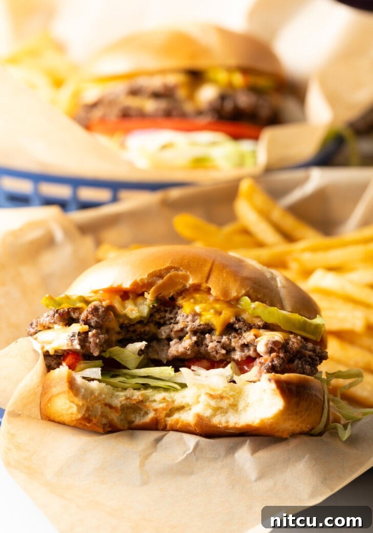Double patty smash burger with cheese, shredded lettuce, and tomato. A large bite has been taken out to show the inside.