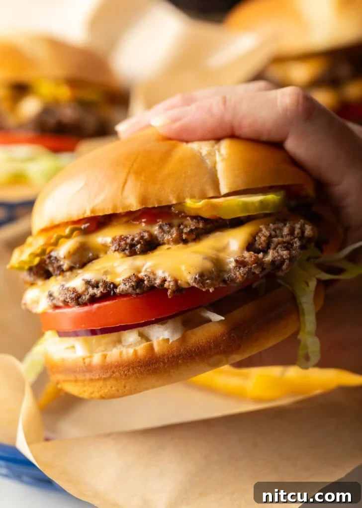 Hand holding double patty smash burger with cheese, shredded lettuce, and tomato.
