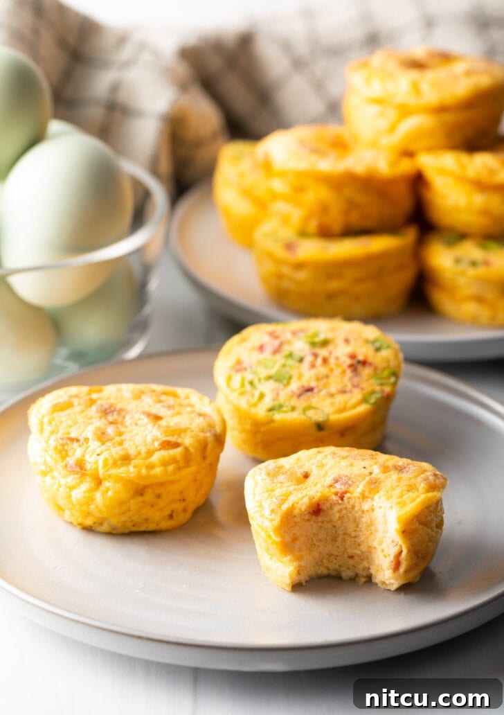 Three golden-brown egg bites on a white plate, one with a bite taken out, revealing its rich, fluffy interior.