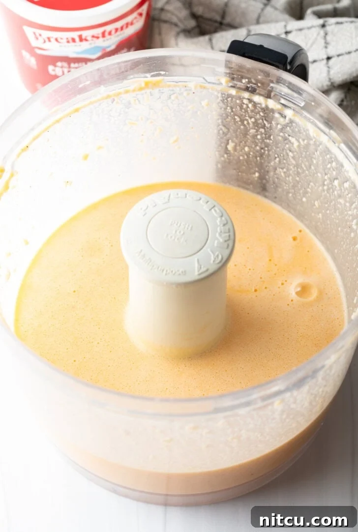 A food processor contains a smooth, light yellow egg mixture, indicating it has been thoroughly blended.