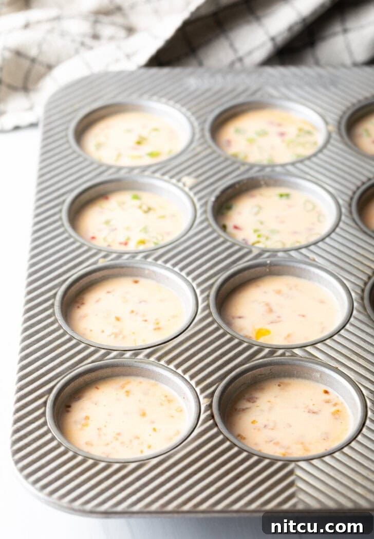 A metal muffin tin holds 12 portions of raw egg blend, ready for baking.