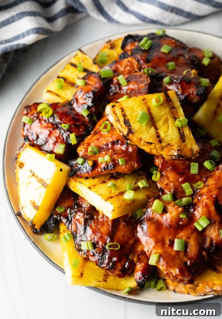 Huli Huli Chicken Recipe - Top down view of sticky chicken pieces topped with chopped scallions and grilled slices of pineapple, showcasing its delicious caramelization.