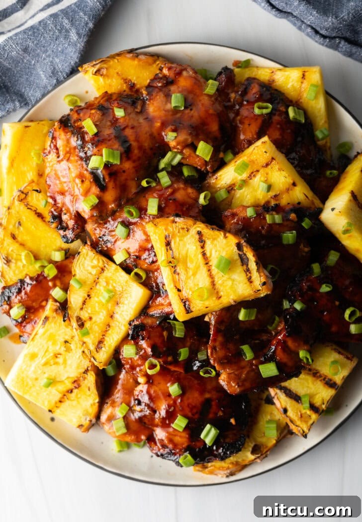 Top down view of sticky huli huli chicken pieces topped with chopped scallions and grilled slices of pineapple, ready to be served.