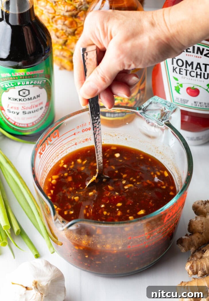 Hand using metal spoon to stir the Hawaiian chicken marinade in a large glass measuring cup, ensuring all ingredients are well combined.