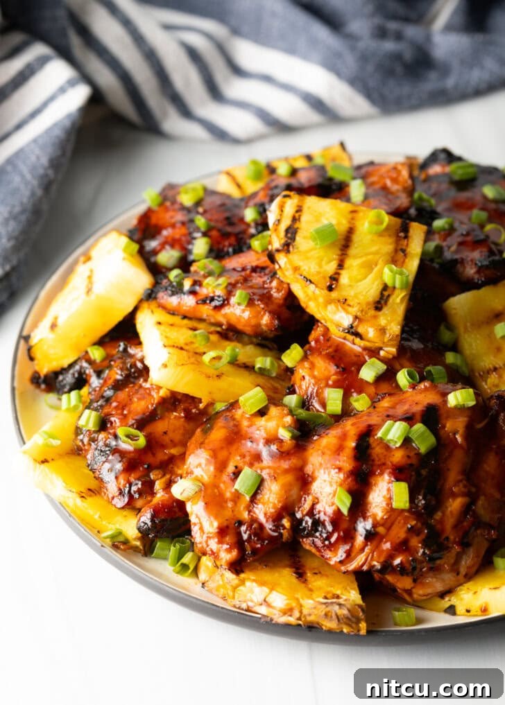 Sticky huli huli chicken pieces topped with chopped scallions and grilled slices of pineapple, showcasing the perfect glaze.