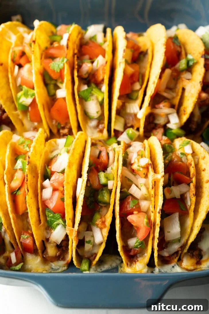 Two rows of a dozen loaded yellow corn hard shell tacos, standing upright in a large baking dish, fresh out of the oven.