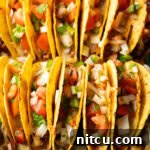 Two rows of a dozen loaded yellow corn hard shell tacos, standing upright in a large baking dish, ready to be served.