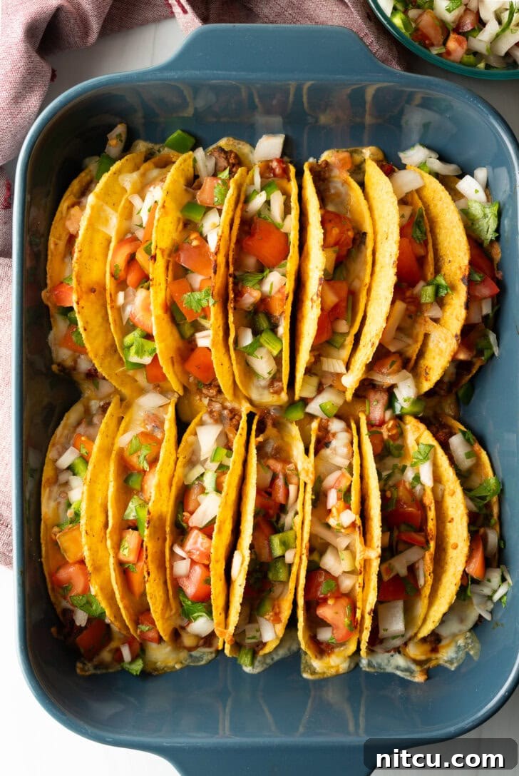 Two rows of a dozen loaded yellow corn hard shell tacos, standing upright in a large baking dish, ready to be served.