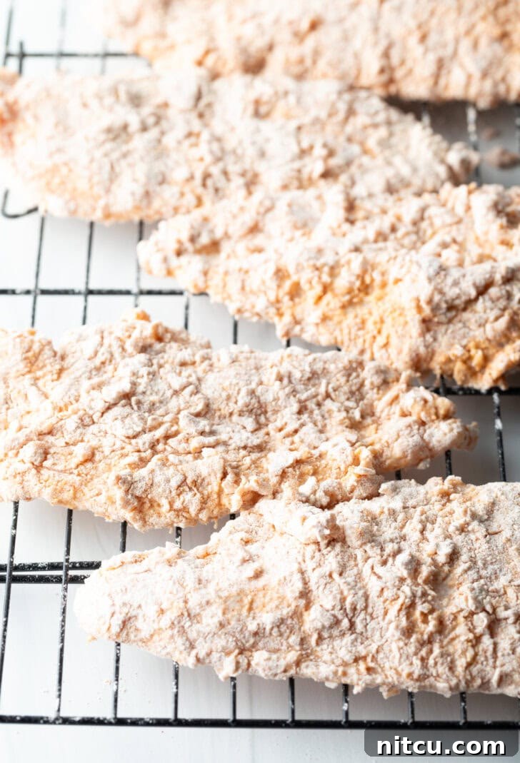Five thinly cut chicken breasts, perfectly dredged and evenly spaced on a wire rack, ready to be fried to a golden crisp.