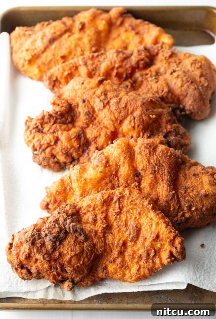 Five pieces of perfectly fried chicken breasts, golden brown and resting on paper towels, allowing excess oil to drain after cooking.