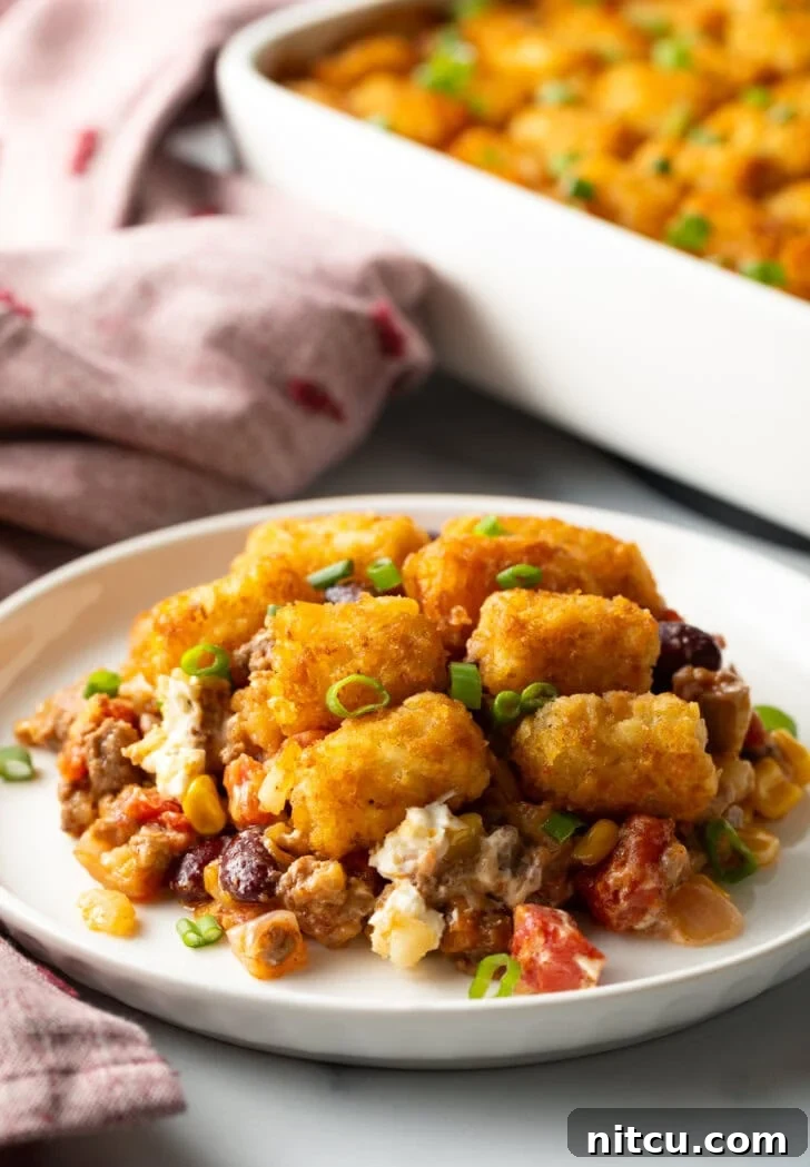 A white plate holding a generous serving of cowboy tater tot casserole, showing the layers of ground beef, cheese, and crispy tots.