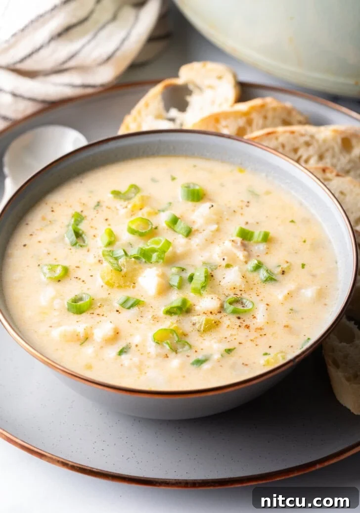 Fish Chowder Recipe in a white bowl, on a gray plate surrounded by slices of bread and a spoon t the side.