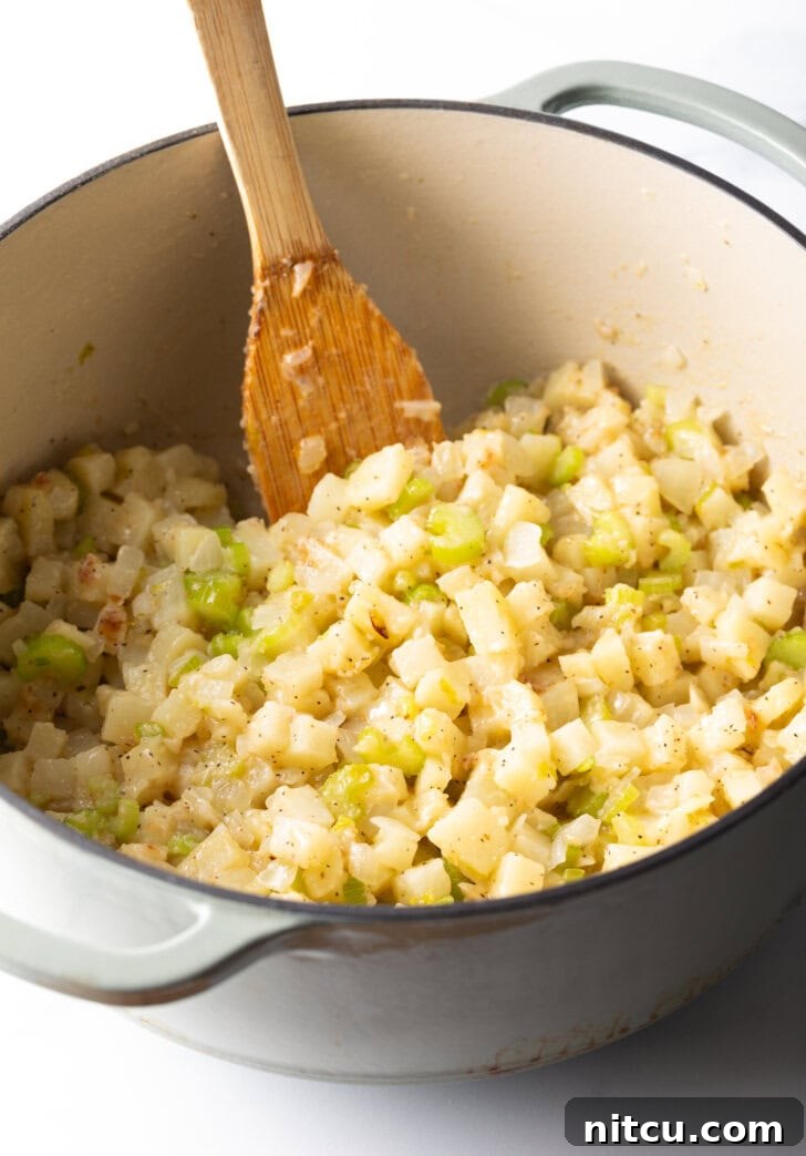Cooking chopped onion, celery, and potato in a large pot with a wooden spatula.
