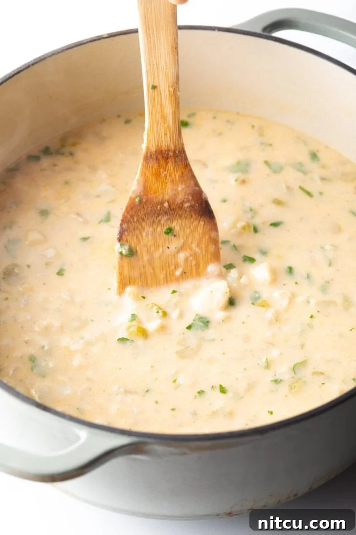 Wooden spatula stirring the fish chowder in a large cooking pot.