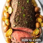 Cooked beef round roast on a metal baking pan. The front half of the roast has been thinly sliced and the meat is surrounded by roasted baby potatoes.