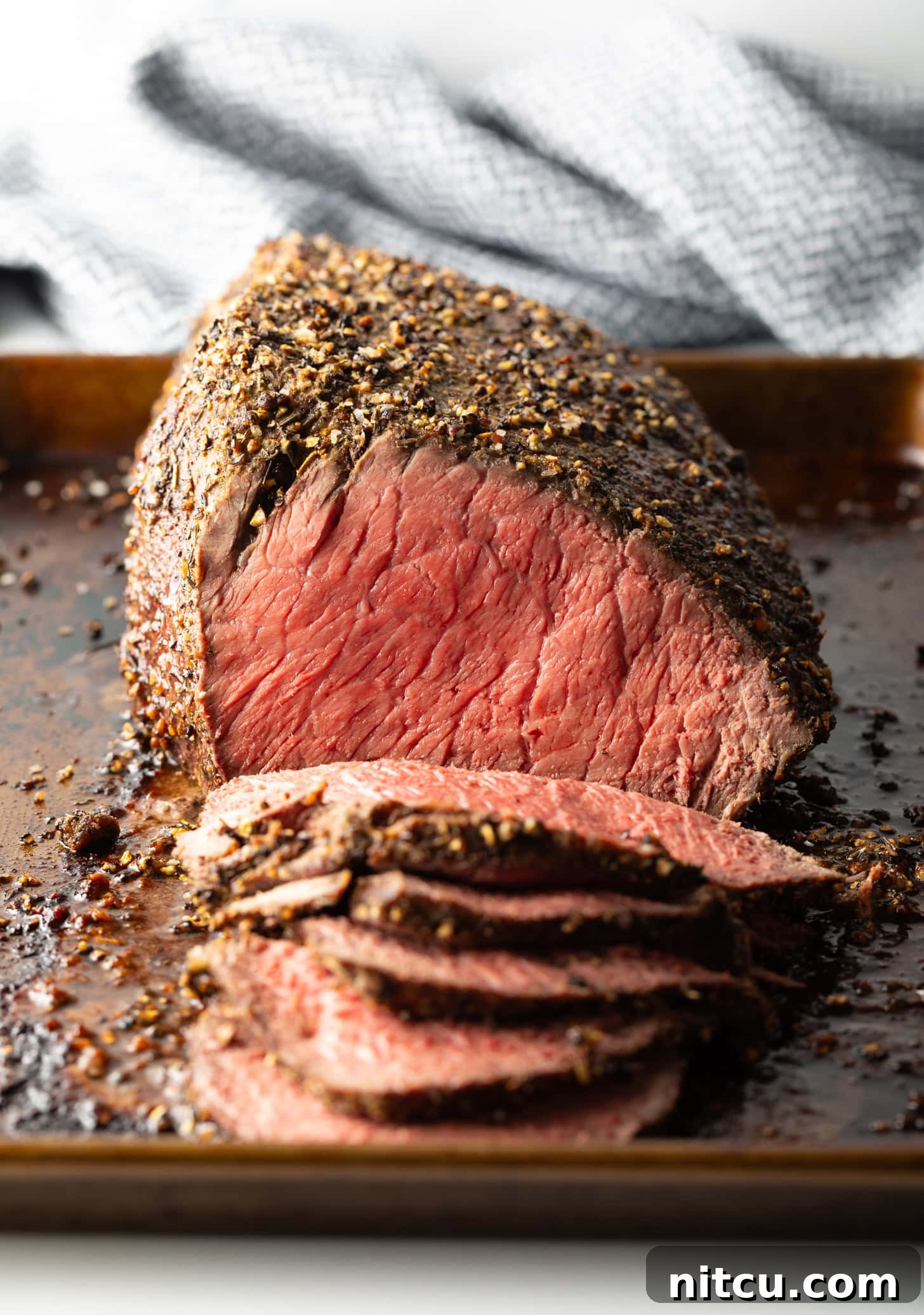 Cooked beef top round roast on a metal baking pan. The front half of the roast has been thinly sliced.