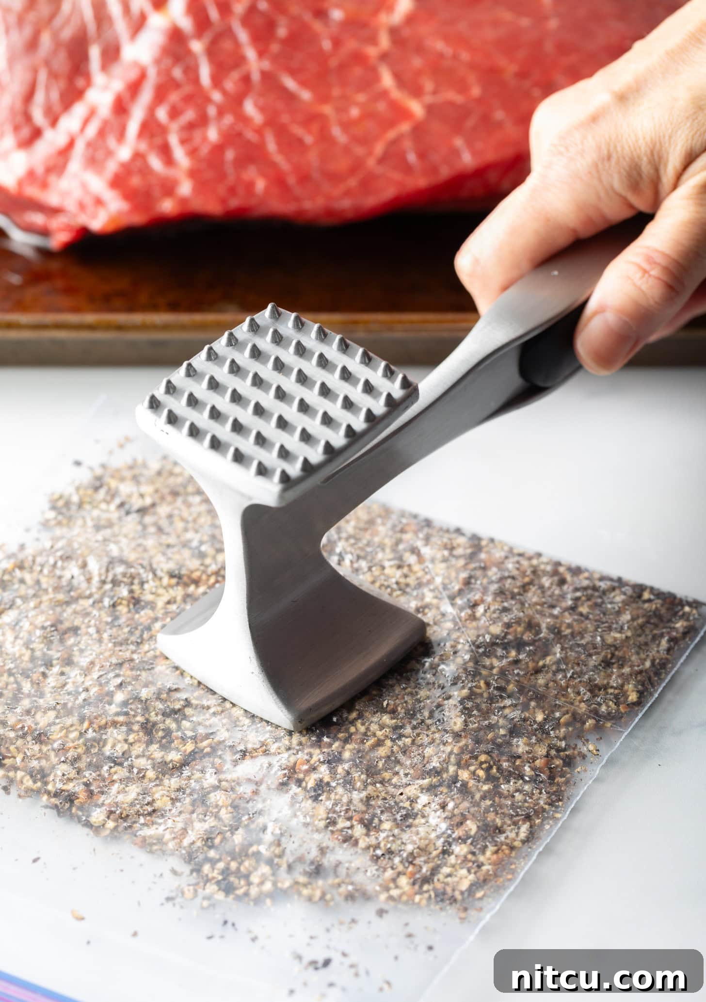 Hand with metal mallet smashed peppercorns in a plastic zipper bag.