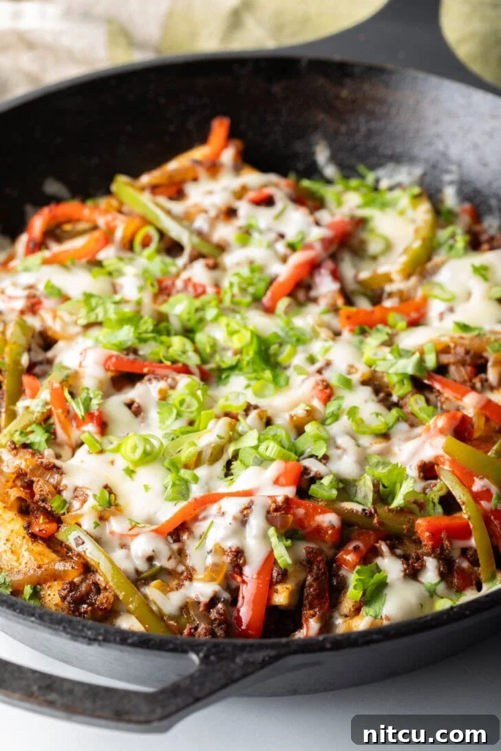 A sizzling skillet of Chori Pollo, featuring seasoned chicken, chorizo, and vibrant peppers, generously topped with melted Monterey Jack cheese and fresh green onions.