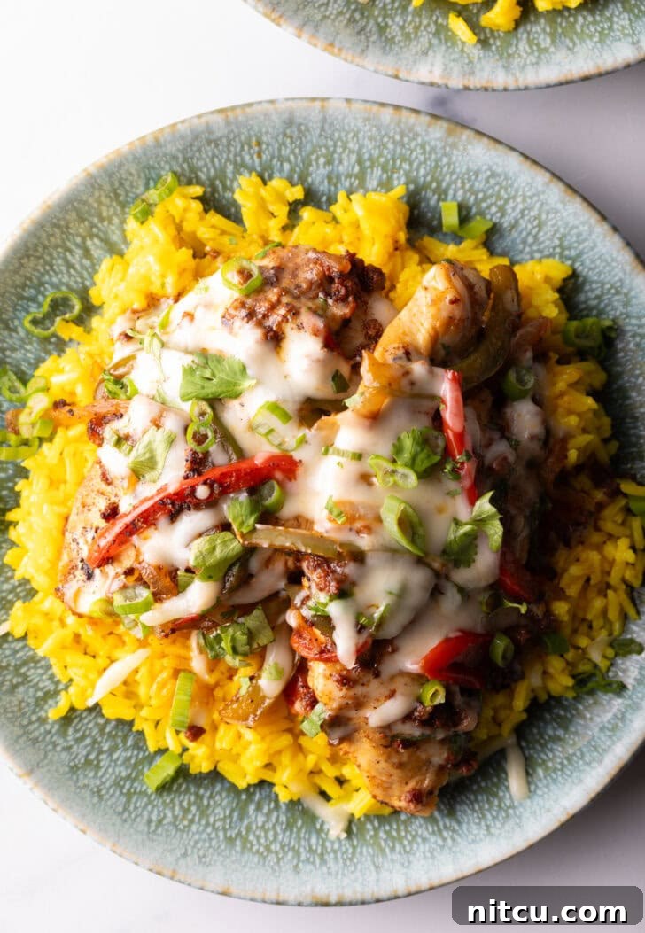 Close-up of a serving of Chori Pollo, golden chicken and crumbled chorizo peeking from under a layer of melted cheese, served atop yellow rice.
