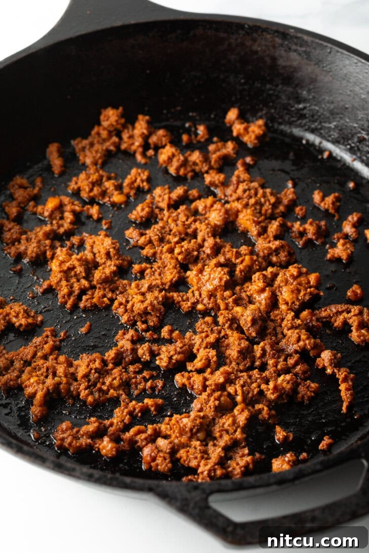 Crumbled Mexican chorizo sausage sizzling and browning in a black cast-iron skillet, filling the pan with its rich, red hue.
