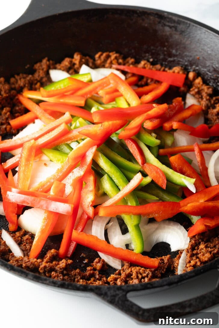 Vibrant sliced bell peppers (red, green, orange, yellow) being added to a skillet, ready to be sautéed in the flavorful chorizo drippings.