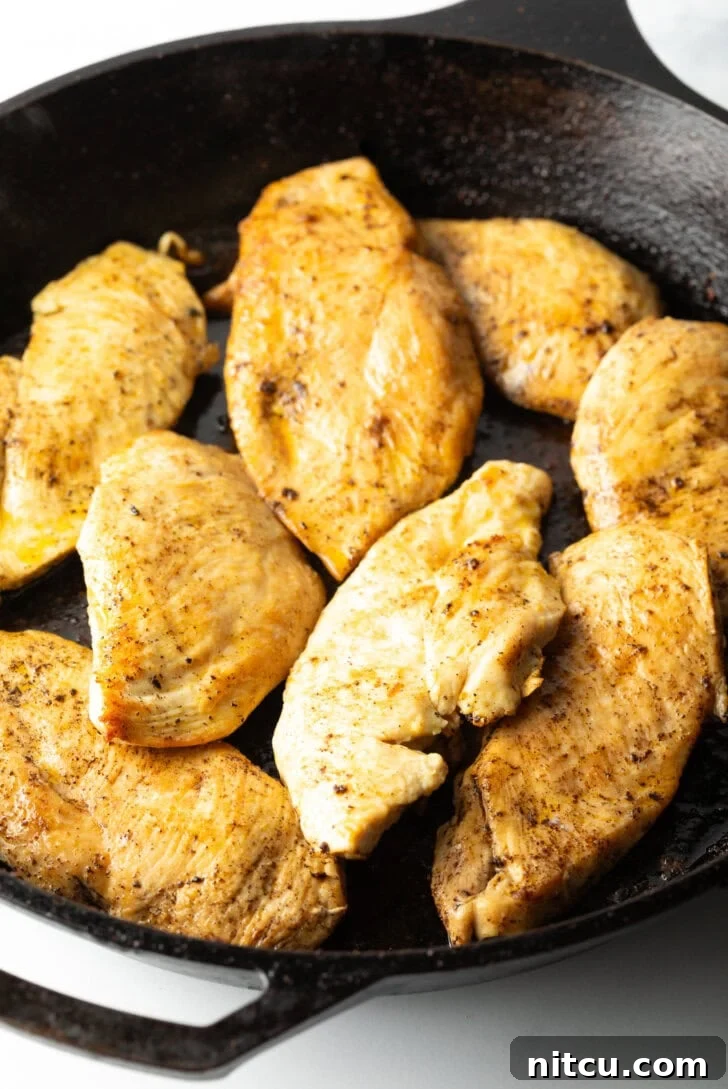 Seven perfectly seared chicken cutlets cooking in a single layer in a hot black cast-iron skillet, achieving a golden-brown crust.