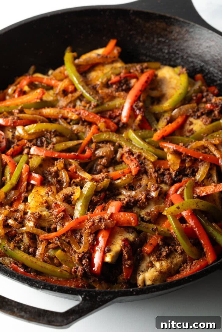 A vibrant mix of yellow, green, orange, and red sliced bell peppers seasoned and ready in a black skillet, creating an aromatic foundation for the Chori Pollo.