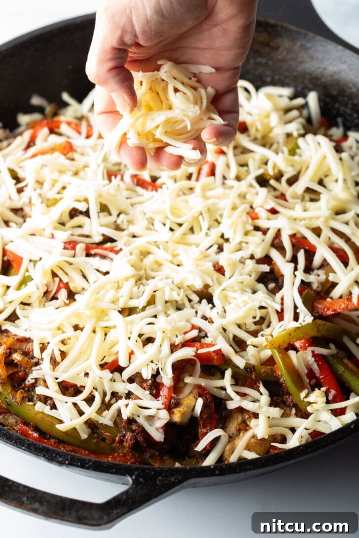 A hand gracefully sprinkles shredded cheese over the simmering chicken and bell peppers in a black skillet, preparing for the melty finish of Chori Pollo.