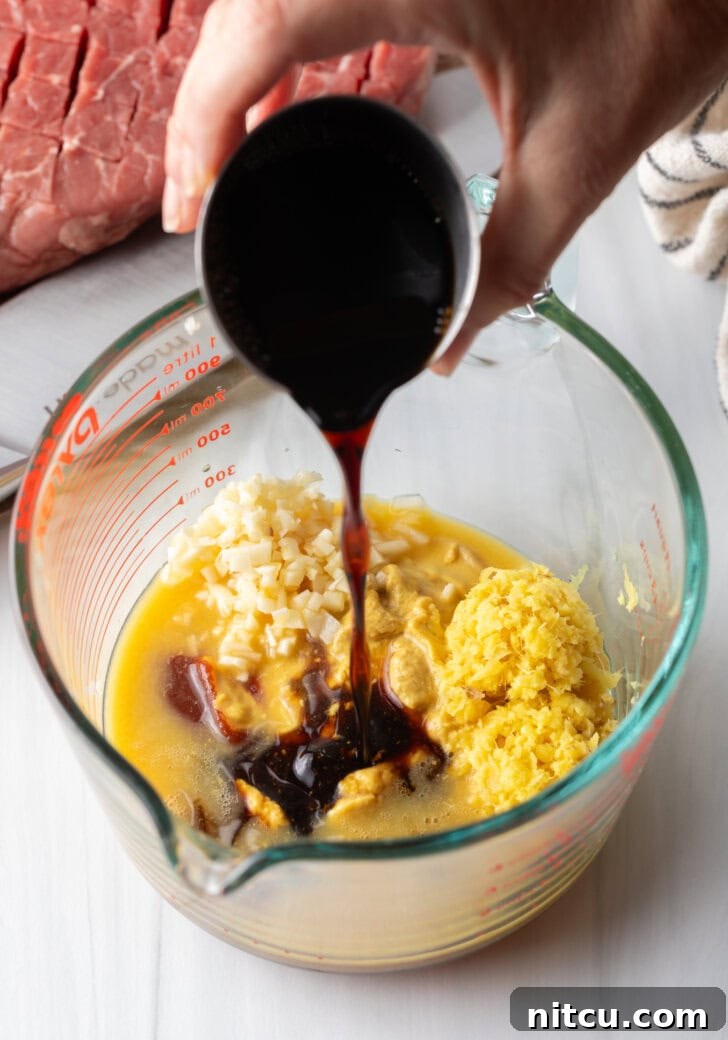 Hand adding dark brown sauce to glass measuring cup with marinade ingredients.