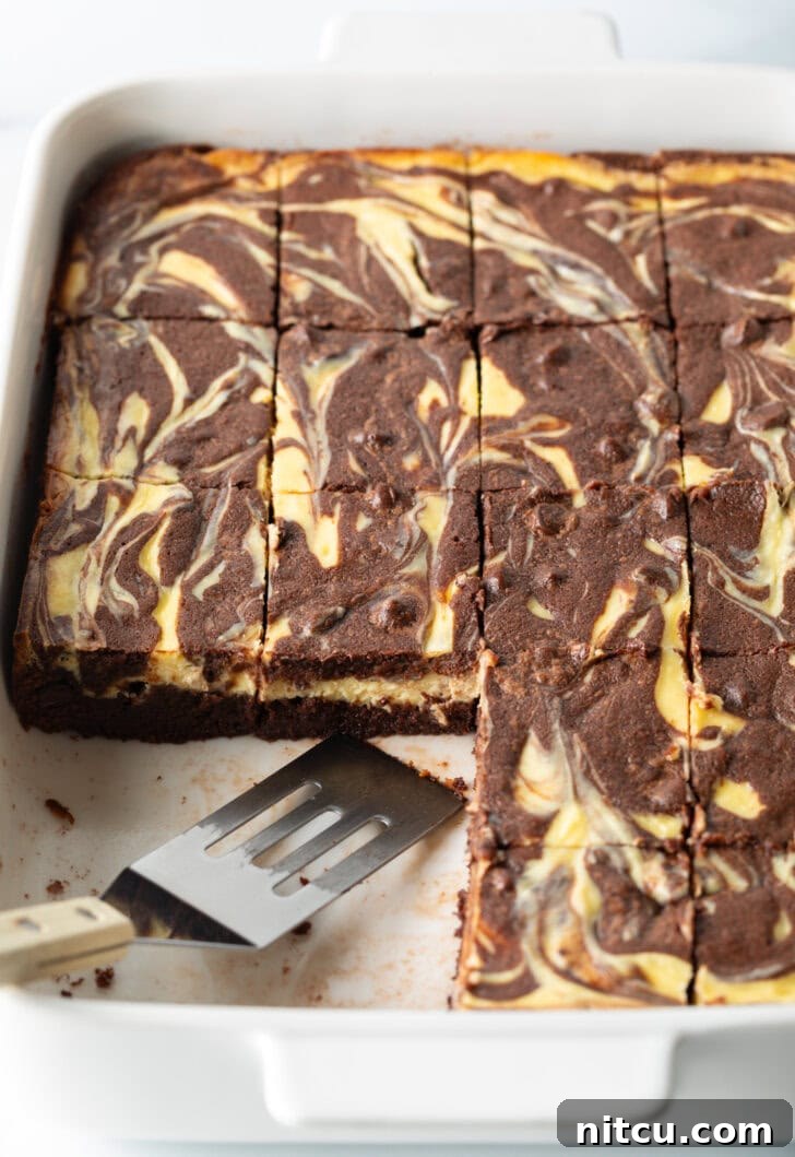 A pan of delicious brownies, with a few pieces already taken, and a metal spatula resting gently in the pan, ready for serving.