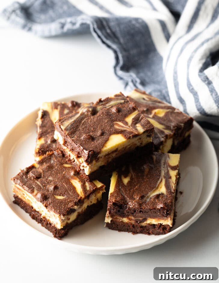 A top-down view of a plate featuring five irresistible cheesecake brownies, with one beautifully stacked on top, showing off its perfect layers.