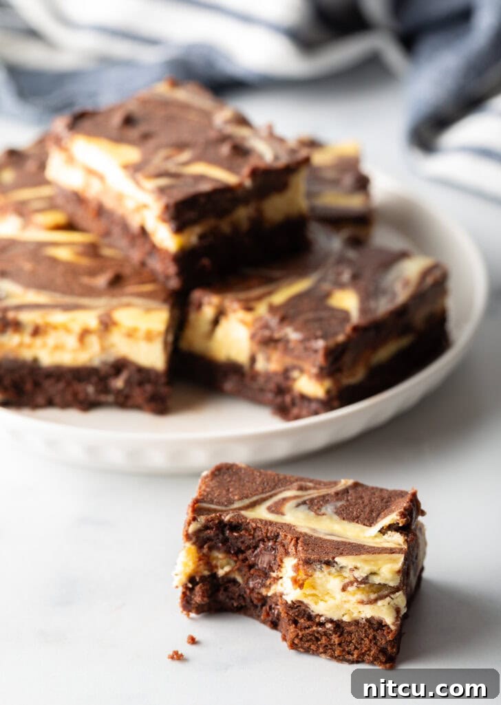 A charming plate displays five cheesecake brownies, with one elegantly stacked, and a sixth brownie positioned closer to the camera for an inviting look.