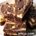 A plate features five delicious cheesecake brownies, with one stacked invitingly on top, highlighting the rich swirl.