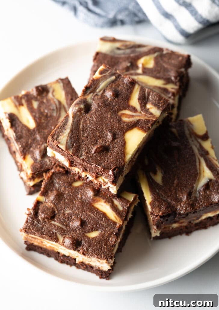 A top-down view of a plate showcasing five decadent cheesecake brownies, with one delicately stacked atop another, highlighting the rich swirl.