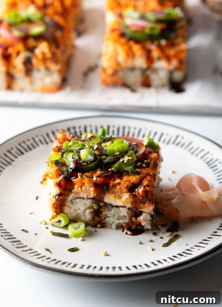 Square of salmon sushi bake on a white plate, garnished with green onions and sesame seeds.