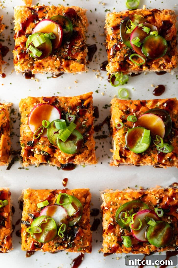 Single square of salmon sushi bake on a white plate, adorned with various colorful garnishes like avocado, cucumber, and radish.