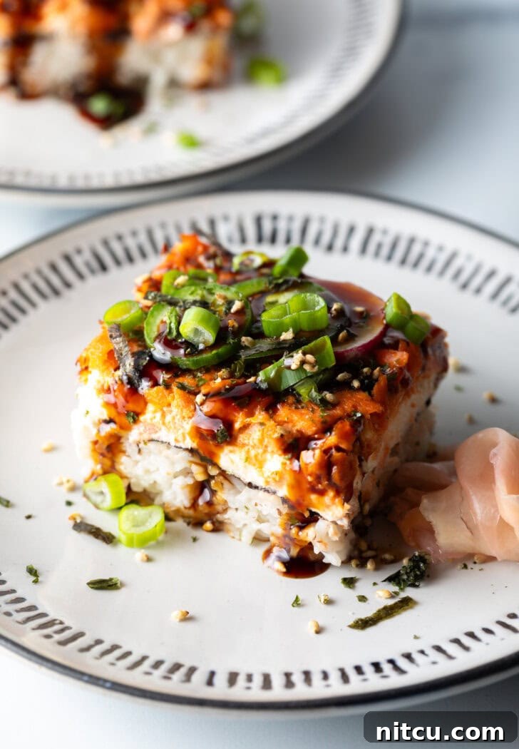 Close-up of a square of salmon sushi bake on a white plate, showcasing the distinct layers and vibrant garnishes, inviting a delicious bite.