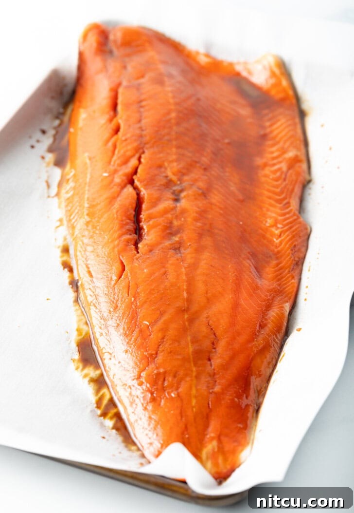 Side view of perfectly cooked salmon fillet resting on parchment paper after baking, ready for flaking.