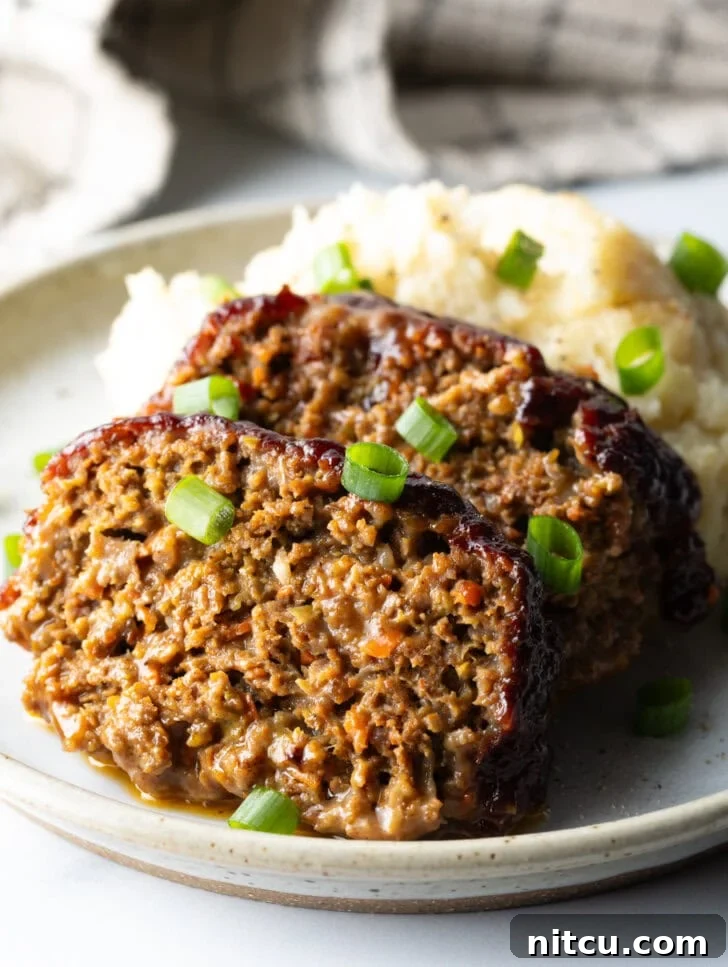 Two generous slices of smoked meatloaf, perfectly browned and glazed, served on a plate alongside a creamy scoop of mashed potatoes, all elegantly garnished with fresh chopped green onions.